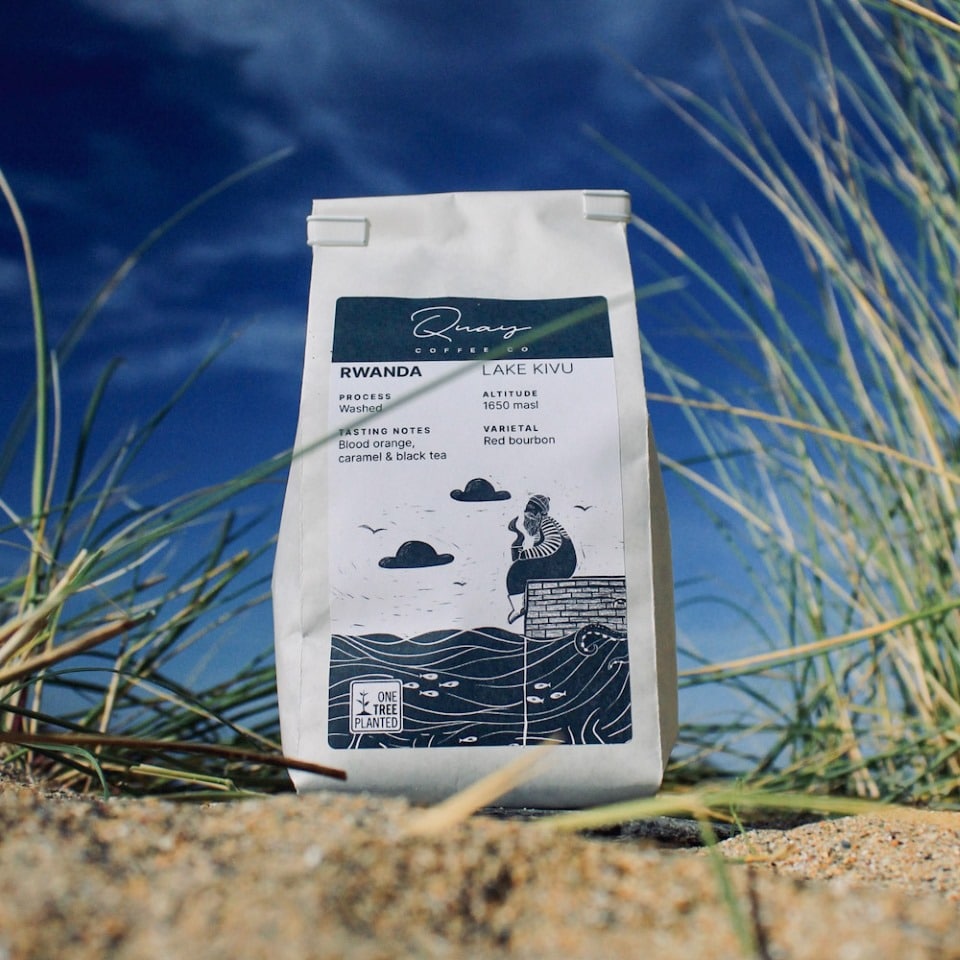 Bag of coffee sits in the sand with grass spiking up around it