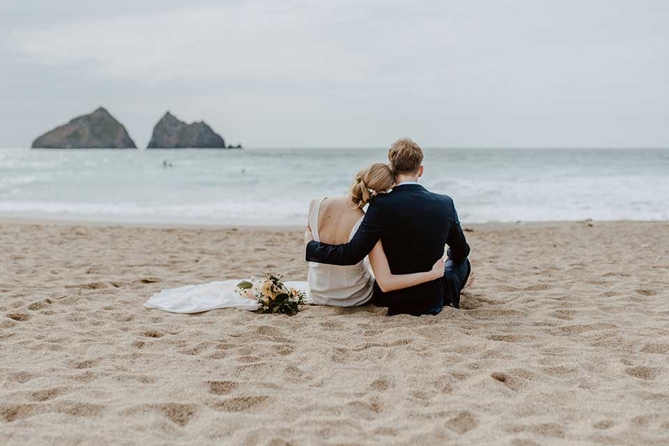 bride and groom sat on the sand in Cornwall