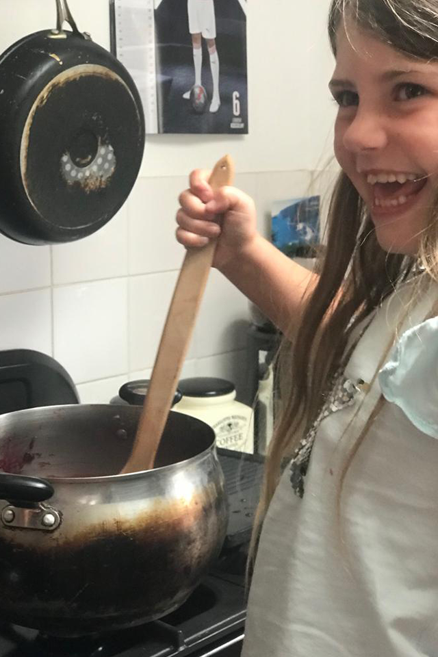 girl stirring homemade blackcurrant jam with wooden spoon