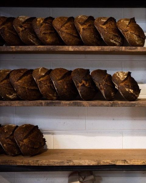 Bread from local produce supplier. Brown and crusty loaves stacked on three shelves.