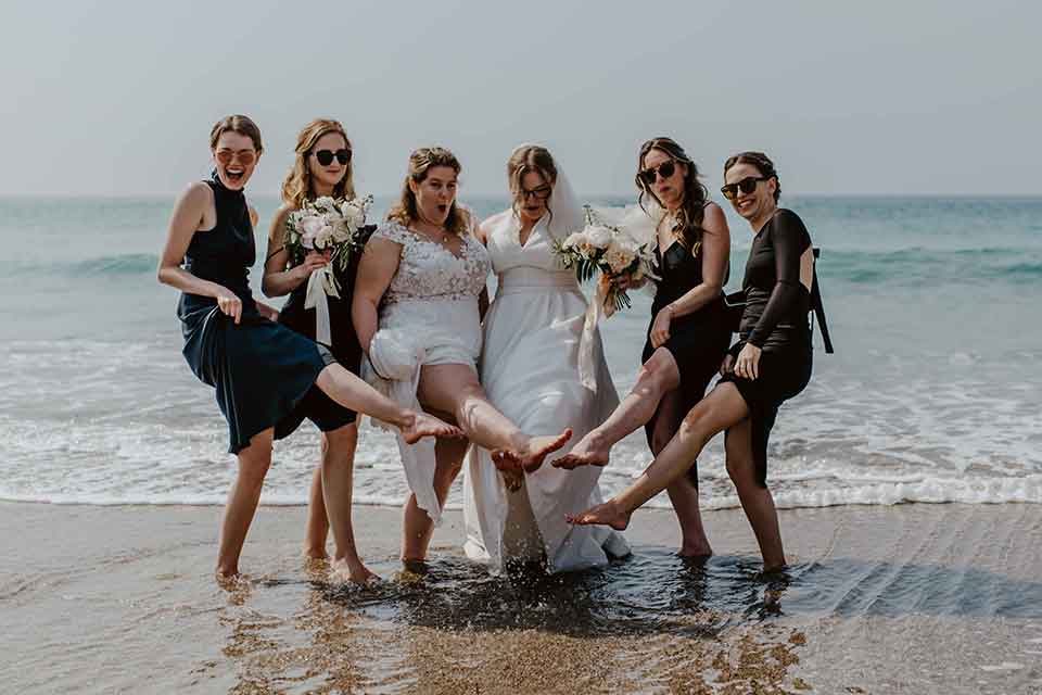 Same sex female wedding couple with bridesmaids on beach