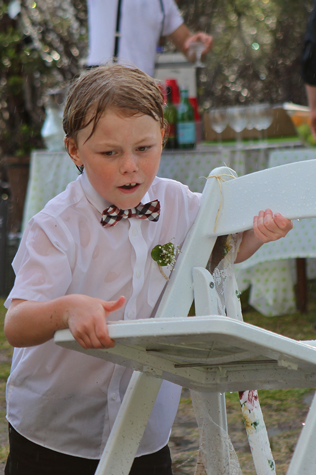 Little boy collection chairs in the rain wedding