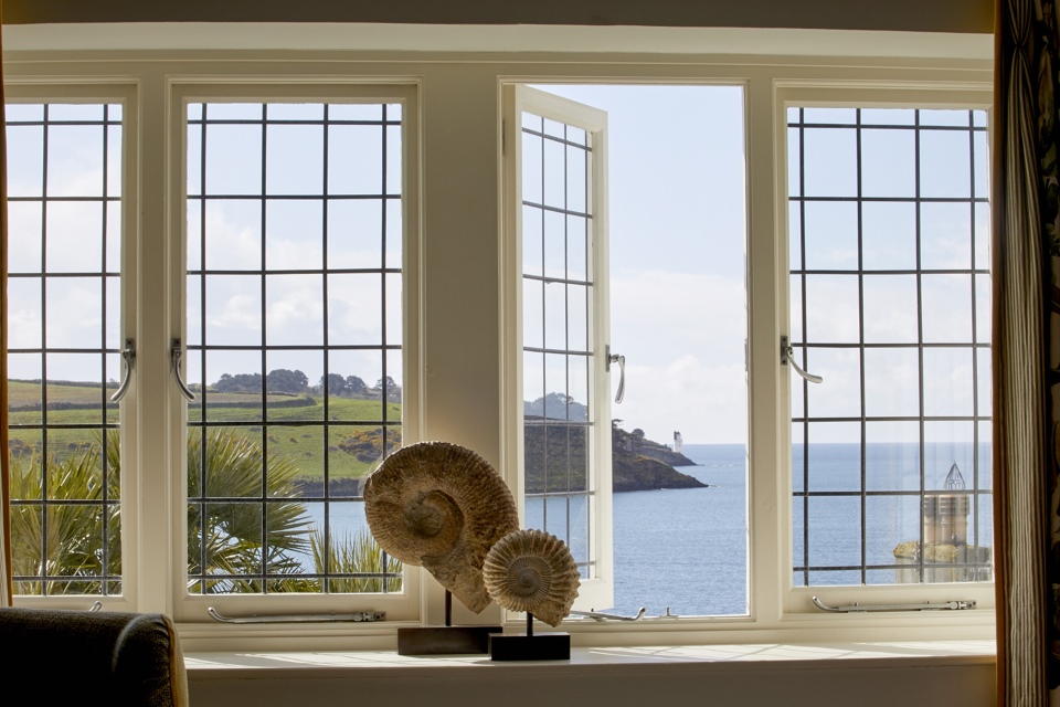 A window overlooks the sea and green hills, with a large shell sculpture in the foreground