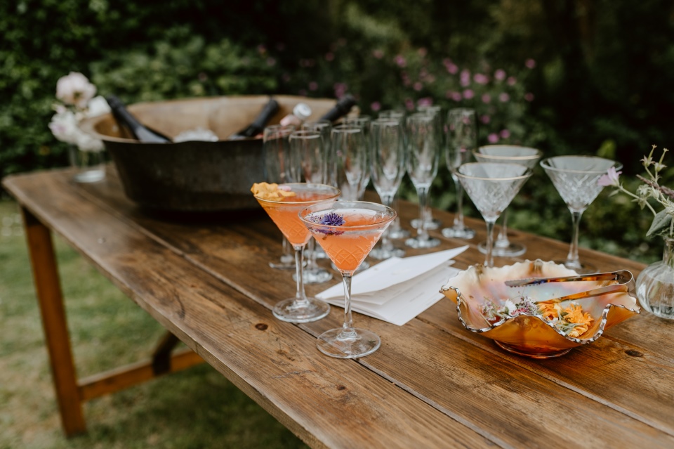 An outdoor bar tabel set up with glasses, pink cocktails and flowers.