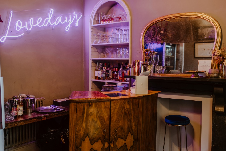 A cocktail bar with wooden accents and a neon bar sign reading Lovedays