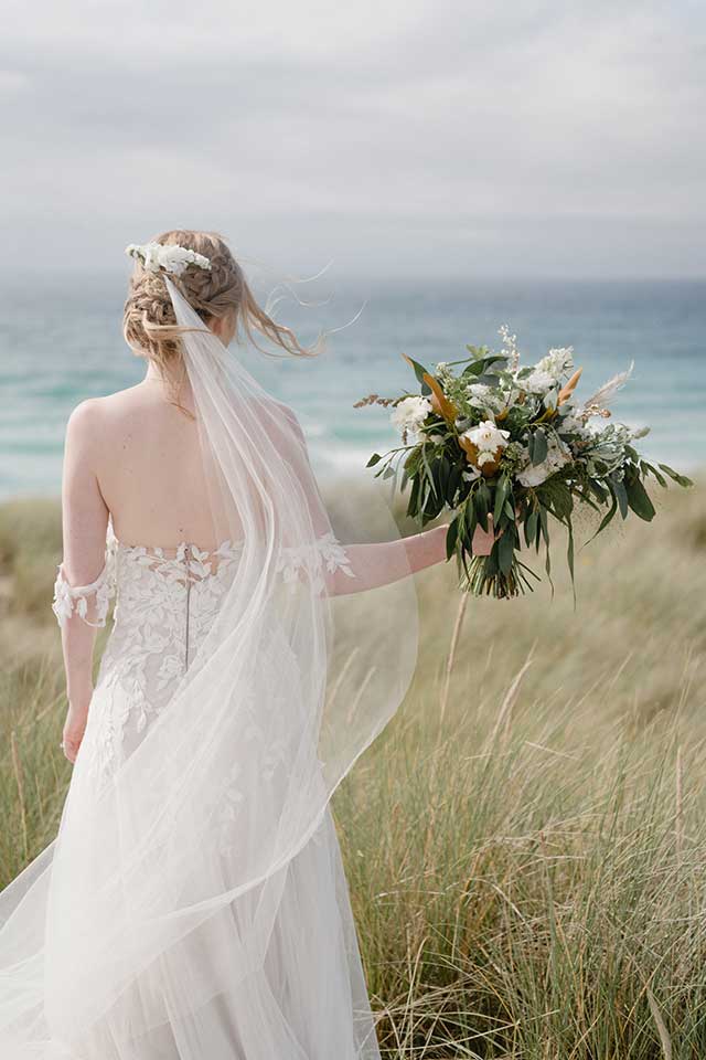 bride in white wedding dress holding bouquet on the beach