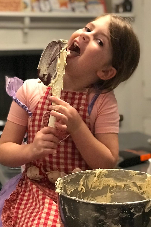little girl baking licking wooden spoon