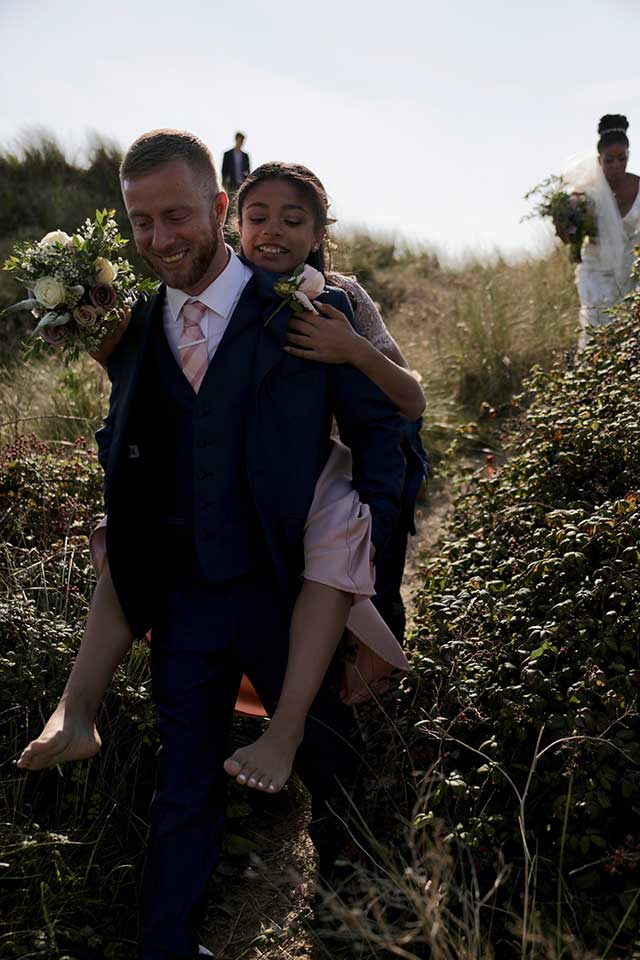 groom carrying daughter across the dunes