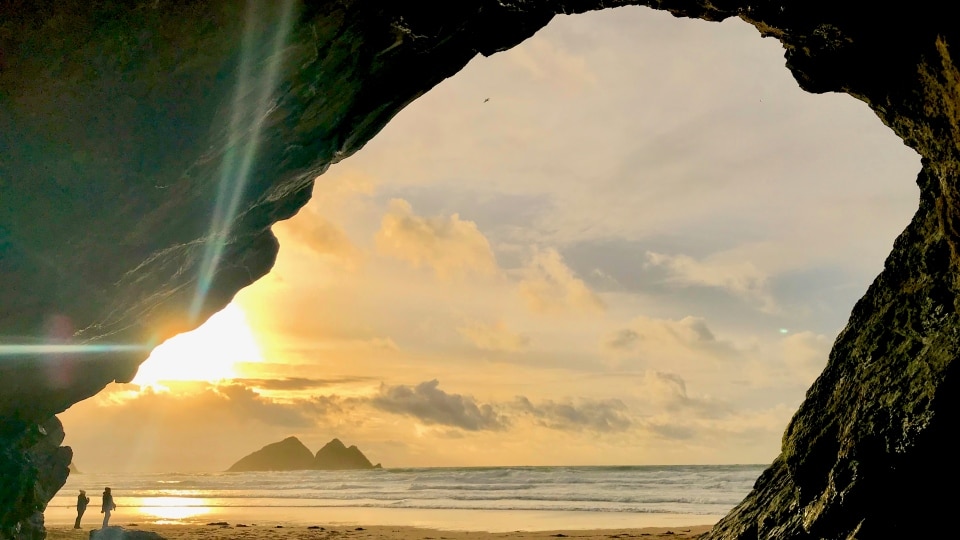Photo from a cave at sunset picturing a rock at sea