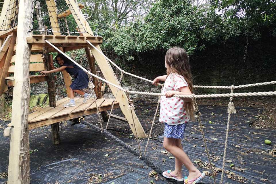 Girl walking across rope bridge on wooden playground